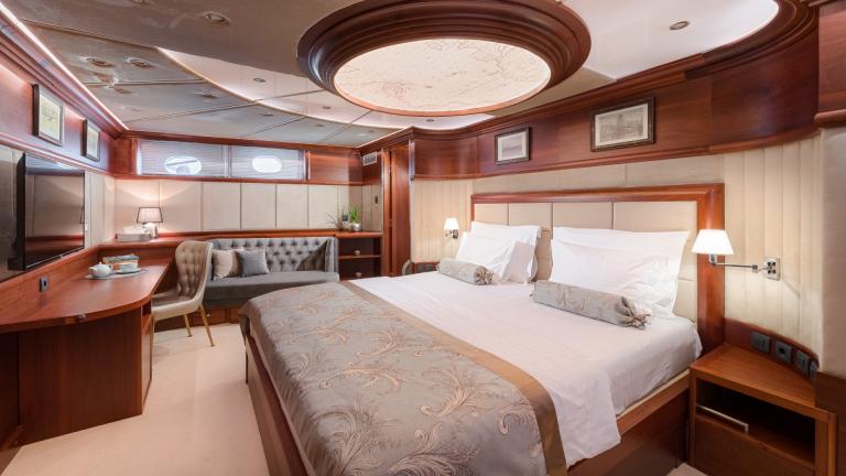 A master stateroom with luxurious double bed, designer couch, desk and TV.